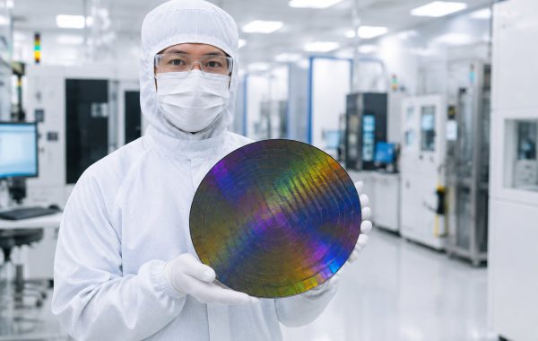Cleanroom technician at TSMC semiconductor fabrication plant holding a 300mm silicon wafer.